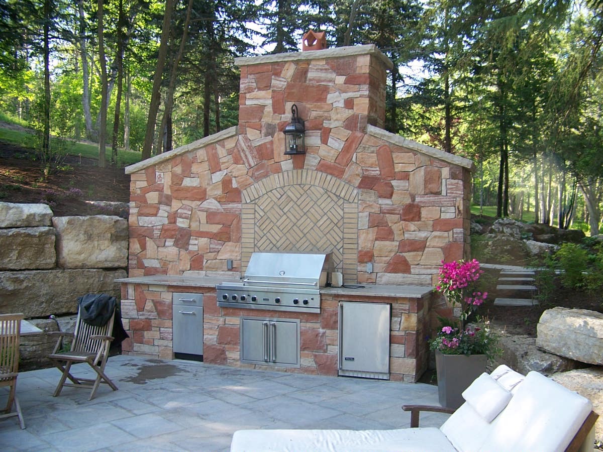 Outdoor stone kitchen with grill in garden setting.