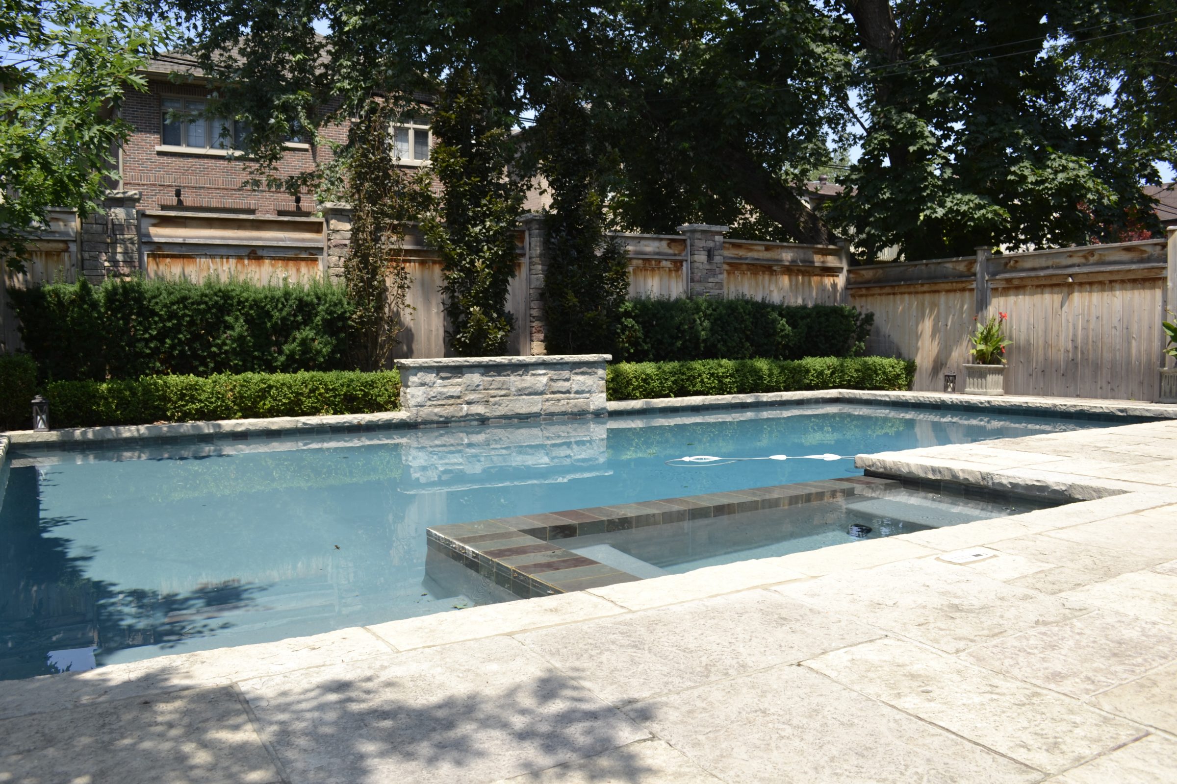 Backyard pool with stone patio and wooden fence.