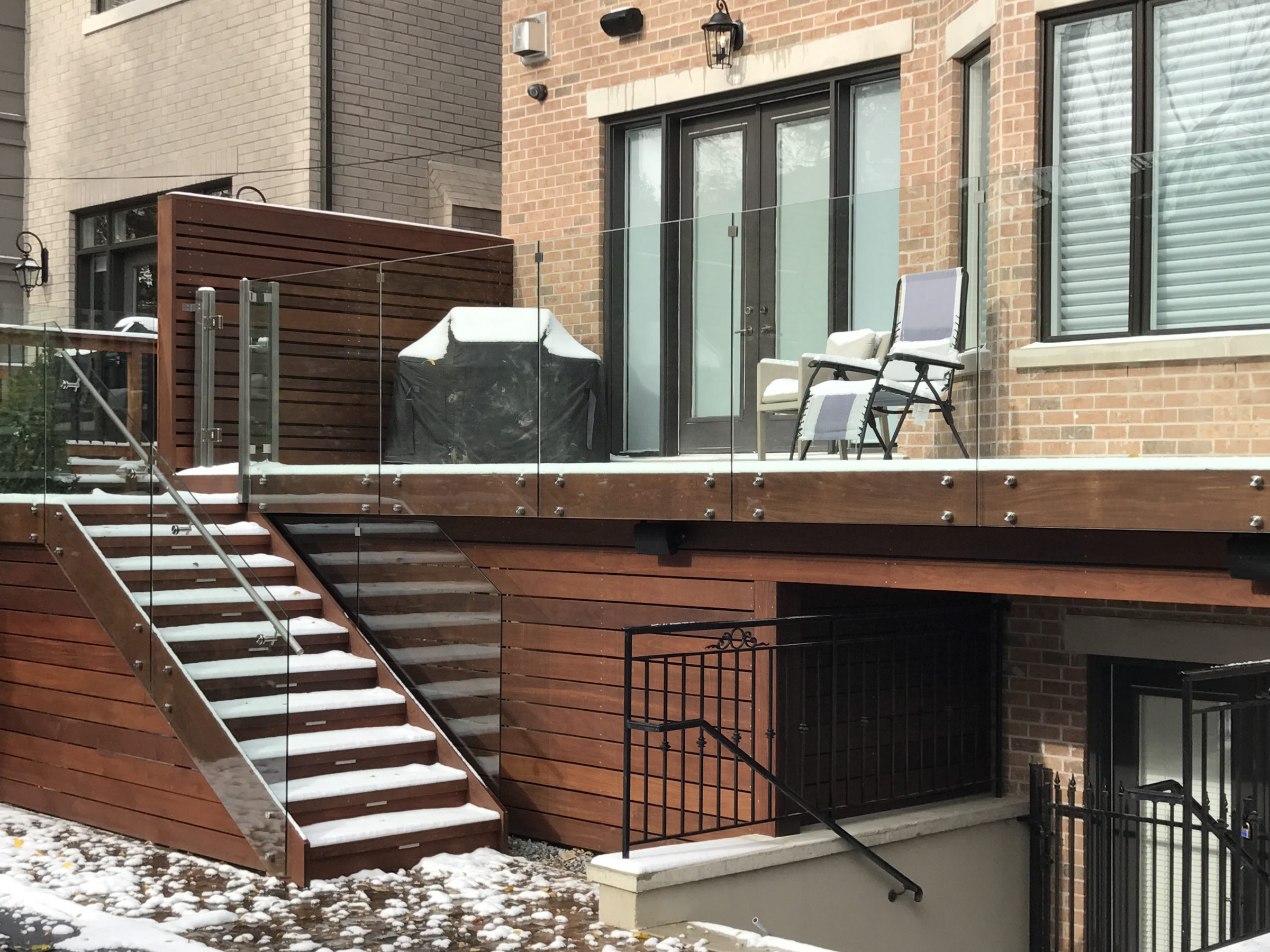 Modern snow-covered deck with stairs and chairs.