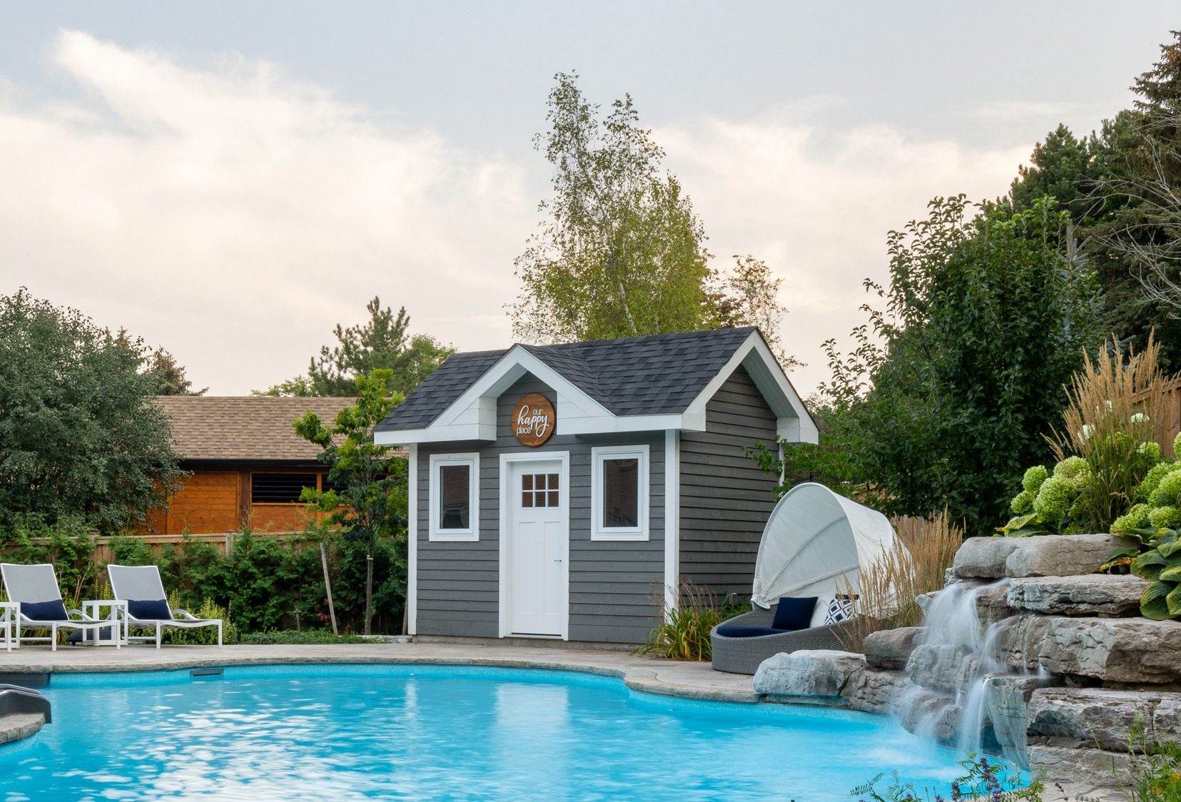 Backyard pool with chairs and waterfall.