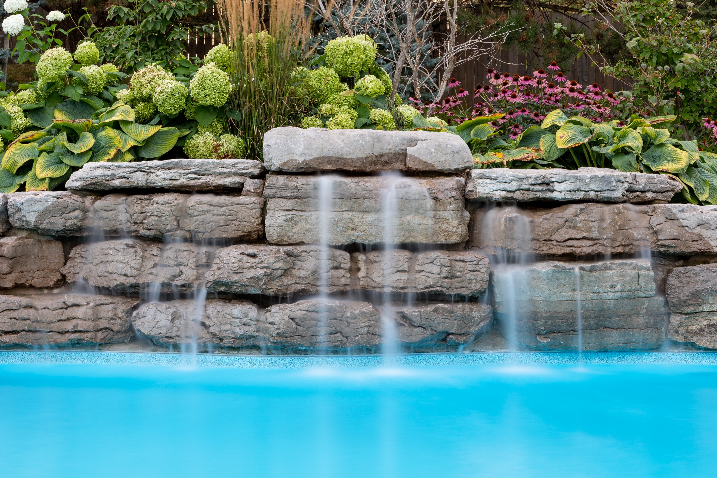 Garden waterfall over rocks into blue pool.