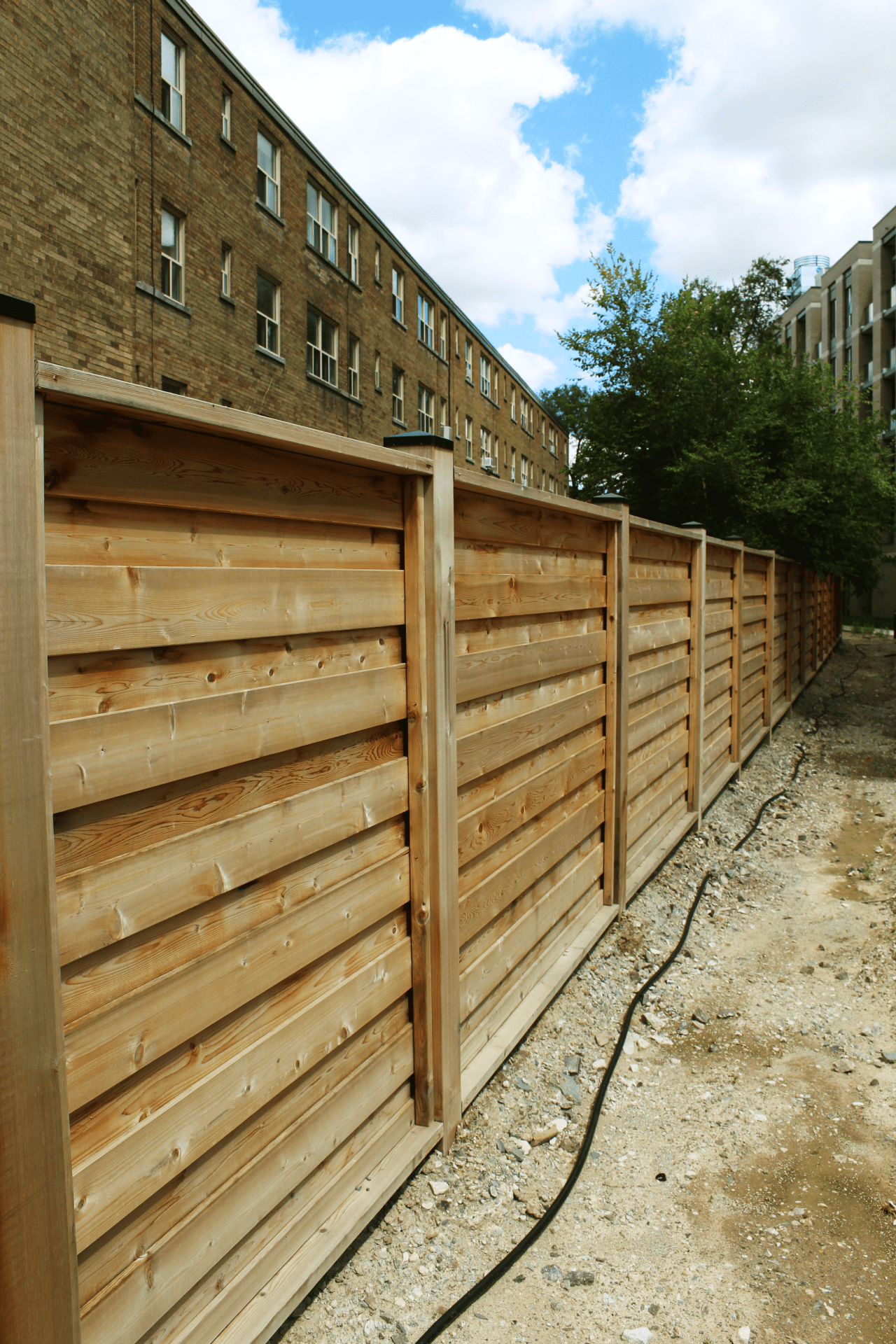 Wooden fence beside a brick building under clouds.