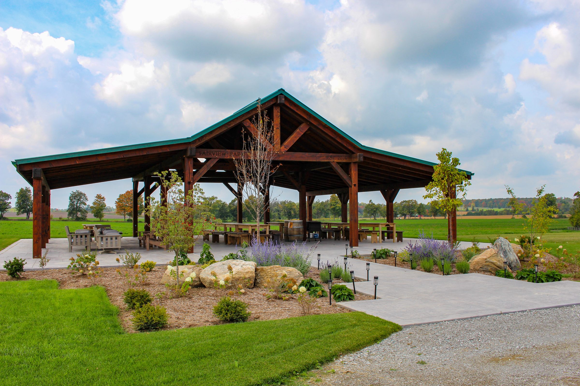 Outdoor pavilion surrounded by greenery and open field.