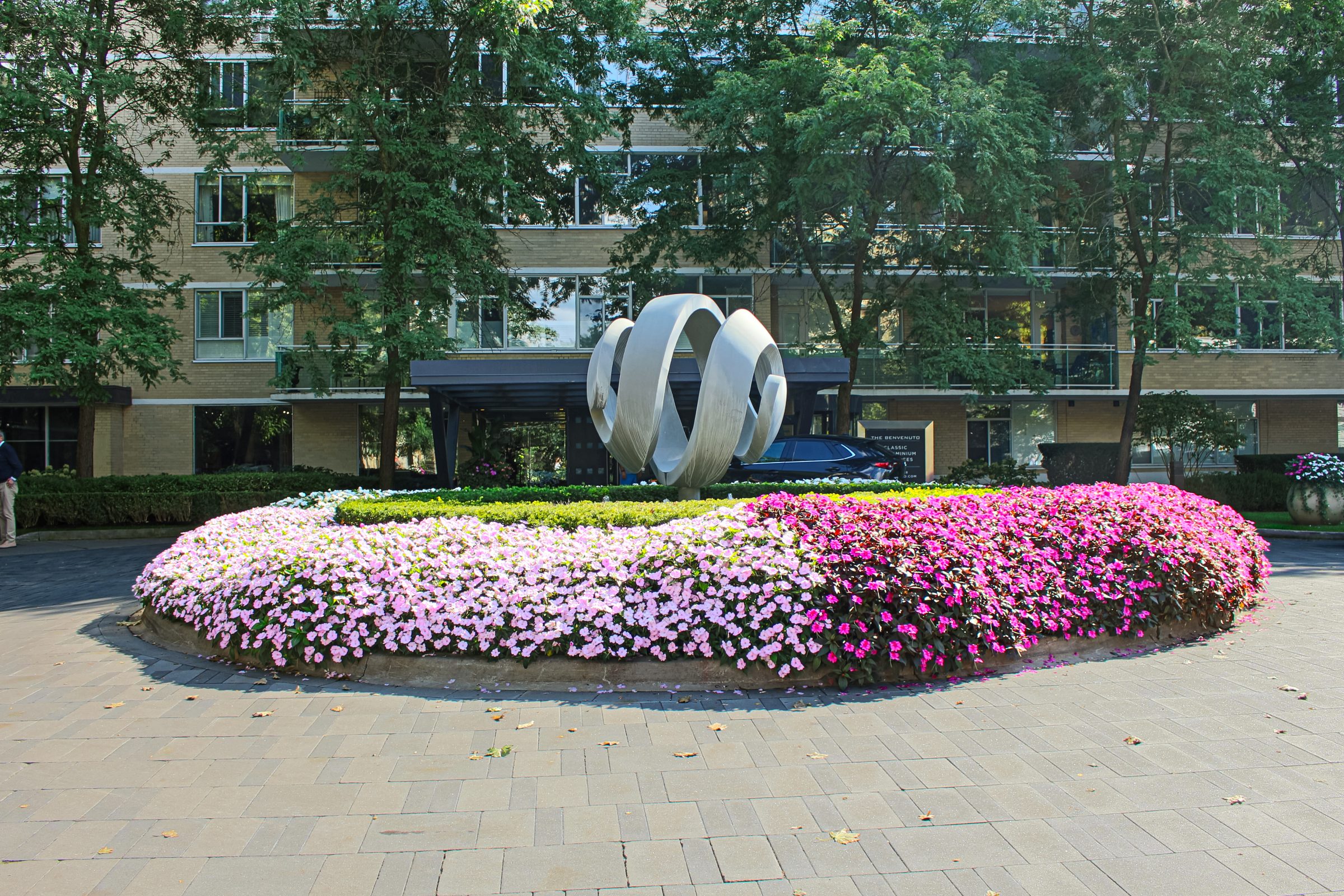 Modern sculpture surrounded by colorful flowers and trees.