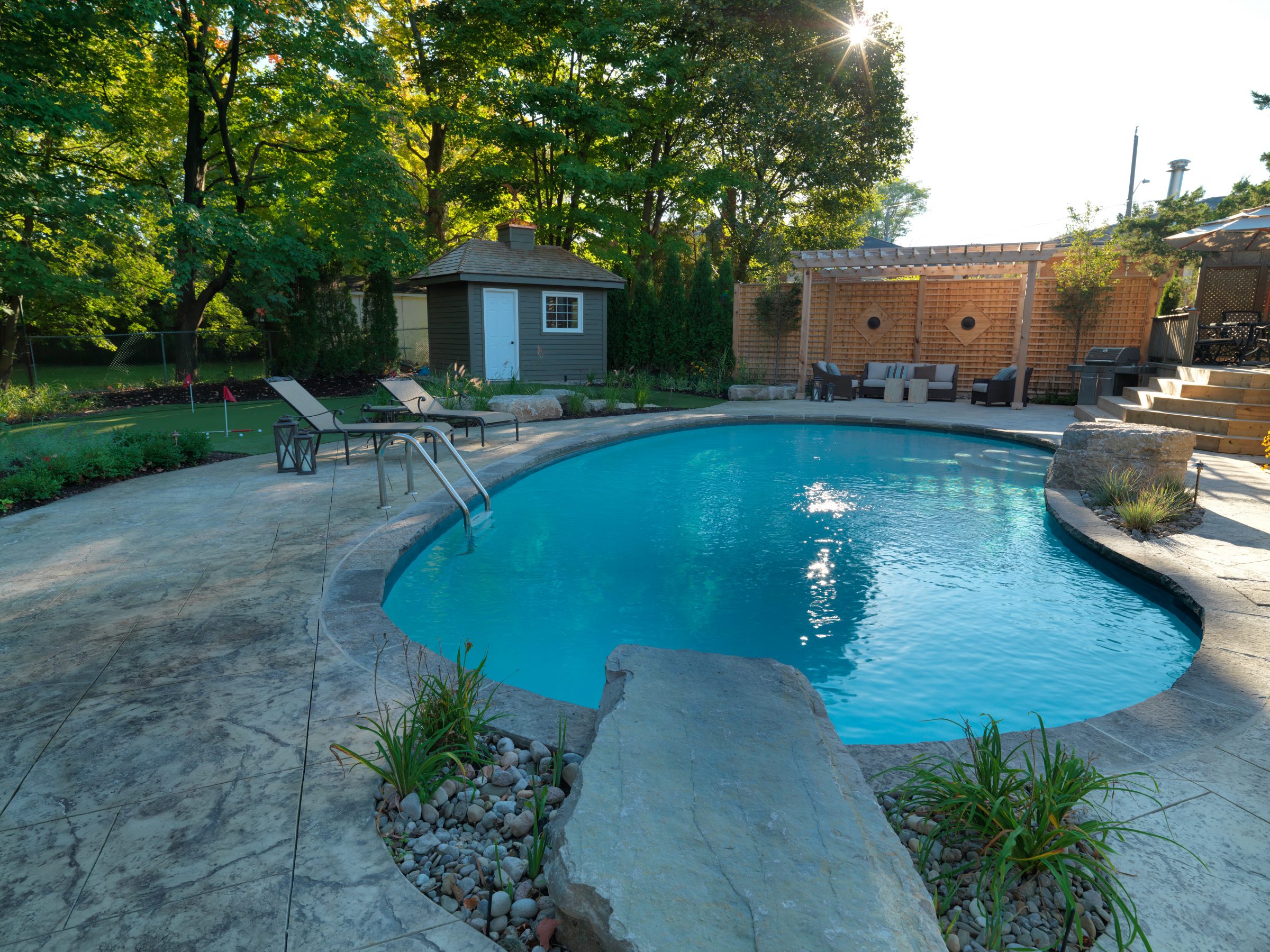 Backyard pool with chairs and stone patio.