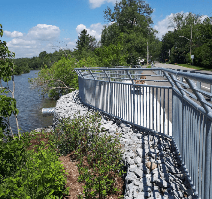 Riverside walkway with metal railing on sunny day.