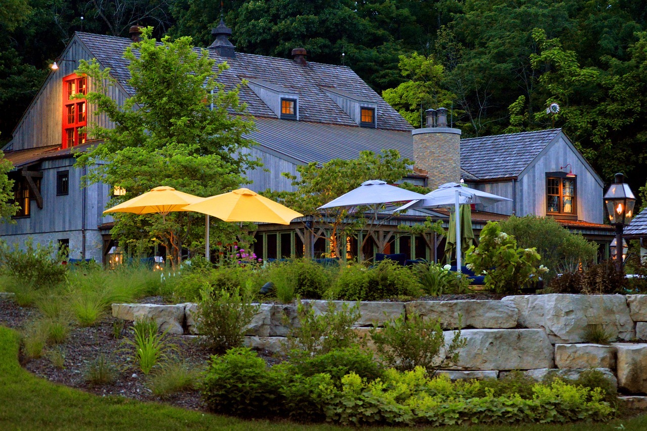 Rustic house with colorful patio umbrellas, lush greenery.