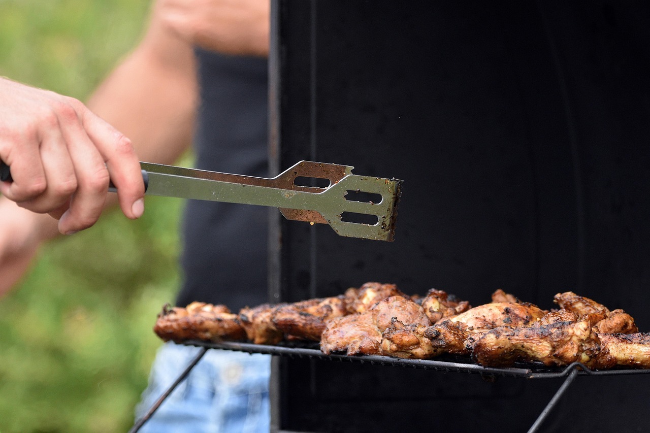 Grilling chicken with metal tongs outdoors.