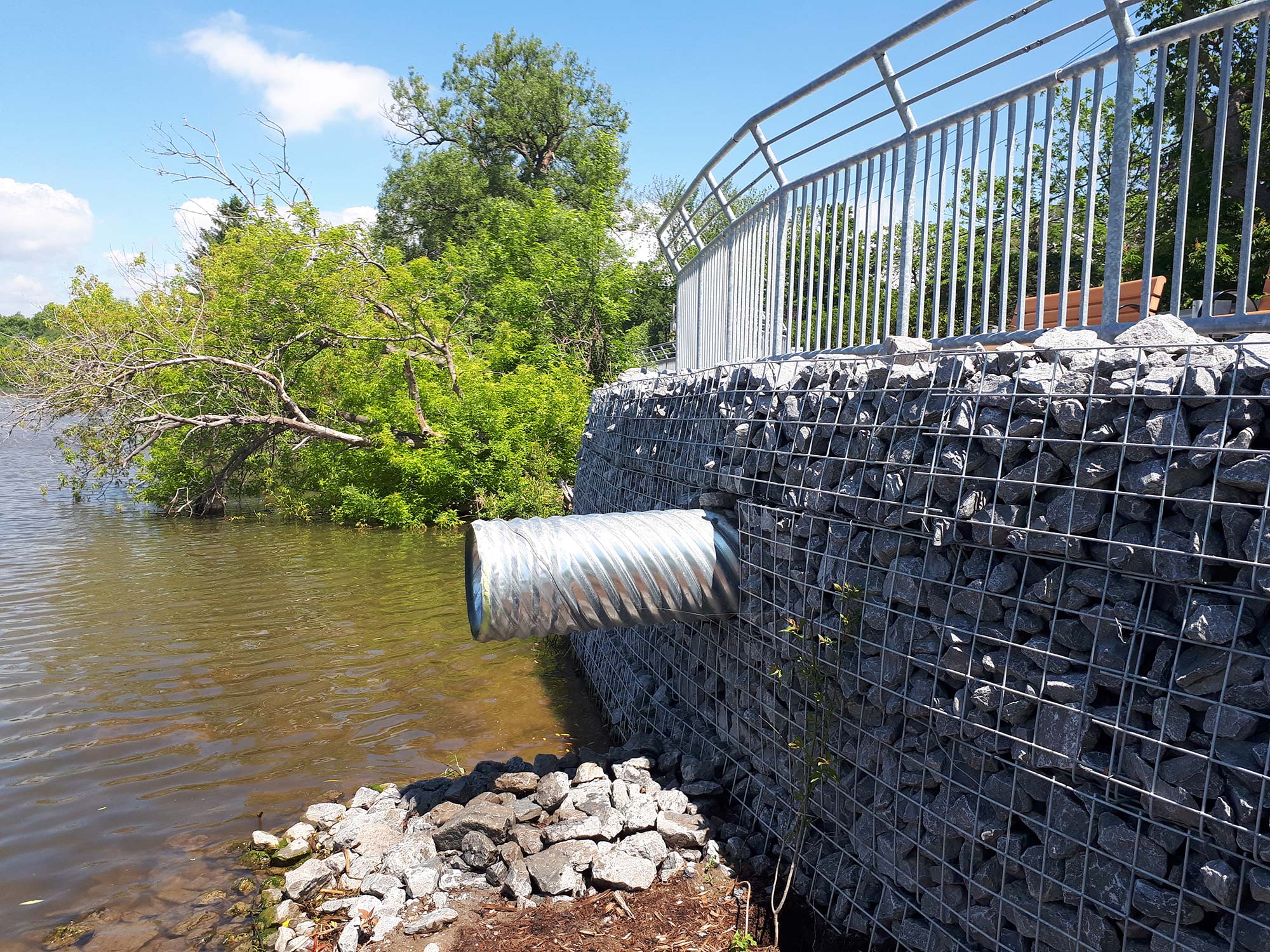 Gabion wall with drainage pipe by a river.