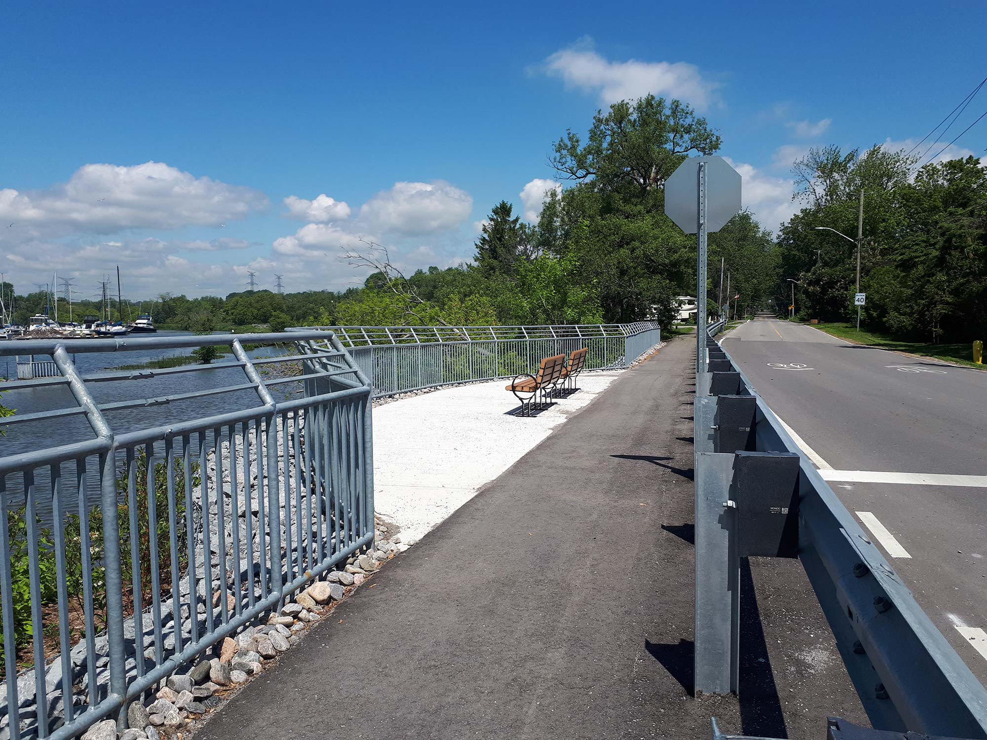 Riverside pathway with benches and trees on a sunny day.