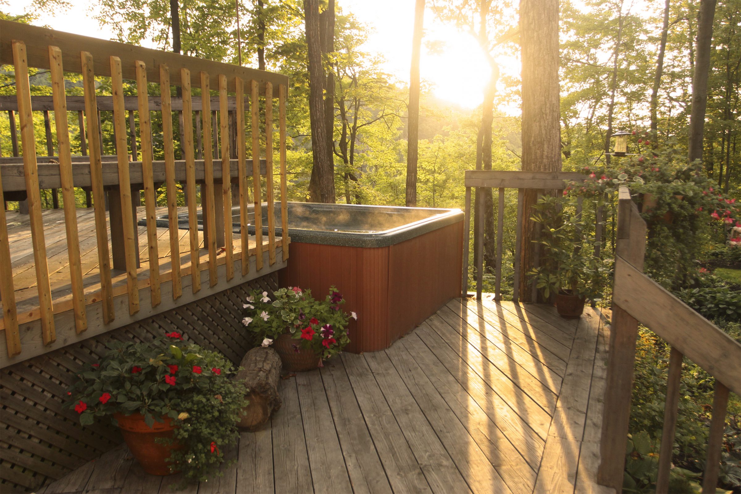 Hot tub on sunny wooden deck amidst trees.