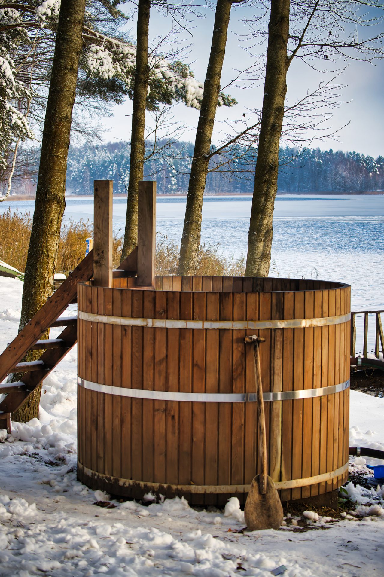 Wooden hot tub beside snowy frozen lake.