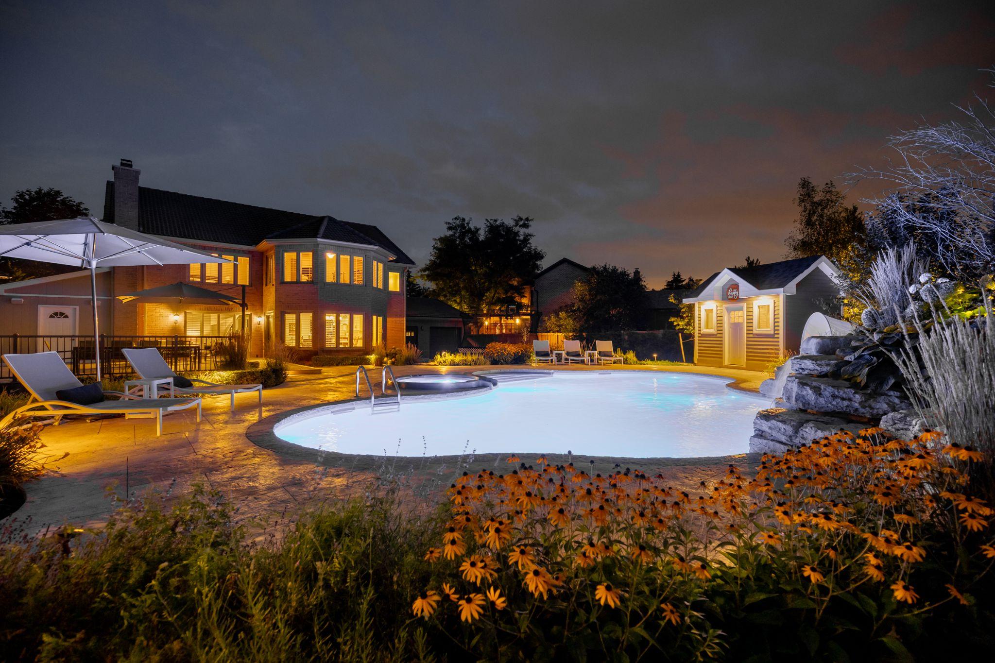 Backyard pool at night with landscape lighting