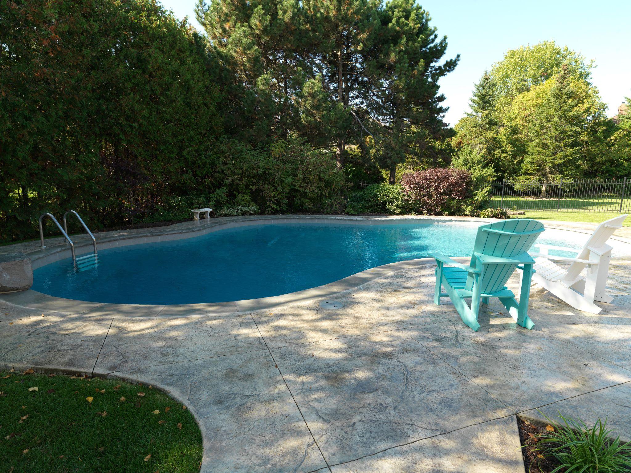 Concrete pool deck with lounge chairs and landscaped yard