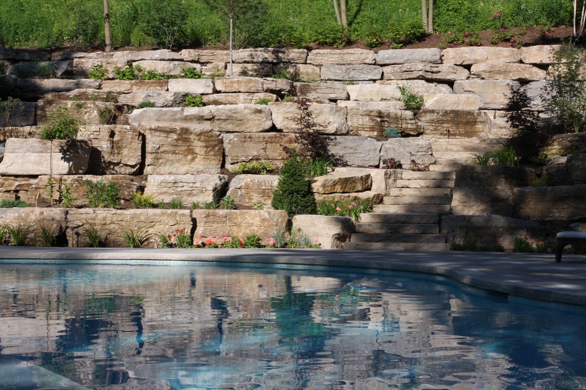 Natural stone retaining wall with steps beside pool
